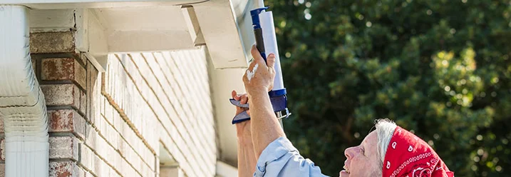 Person verwendet Dichtmittel an Dachrinne